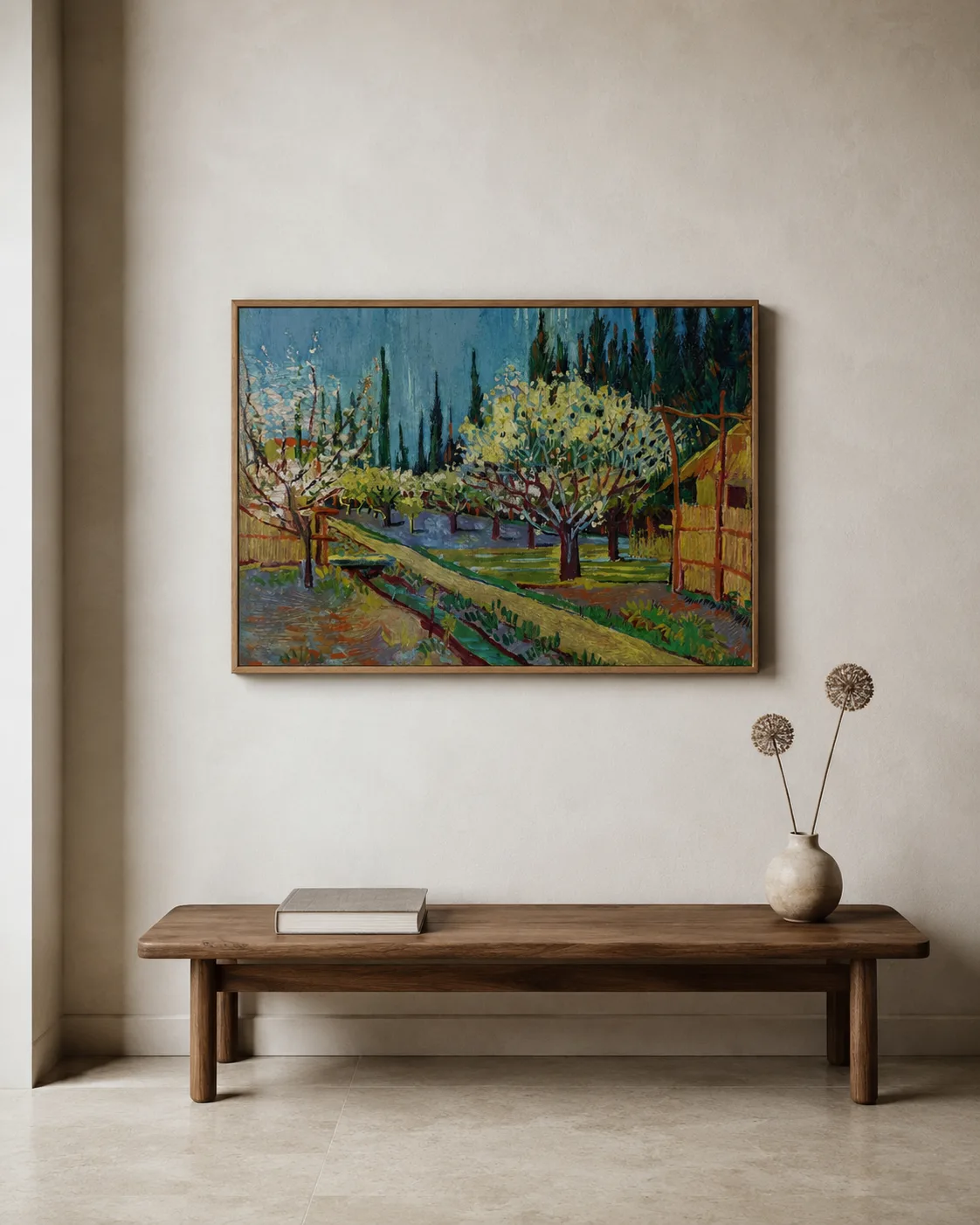 A framed Van Gogh orchard landscape print above a low oak bench with a closed book and dried allium stems